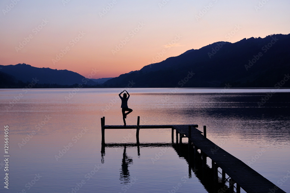 Junge Frau am See praktiziert Yoga nach Sonnenuntergang