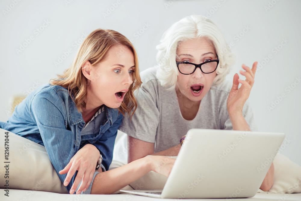 Emotional surprised woman and her adult daughter resting at home Emotional surprised woman and her adult daughter resting at home