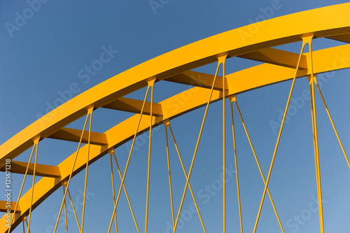 Yellow bridge against a steel blue sky showing beams, girders, columns and cables photo
