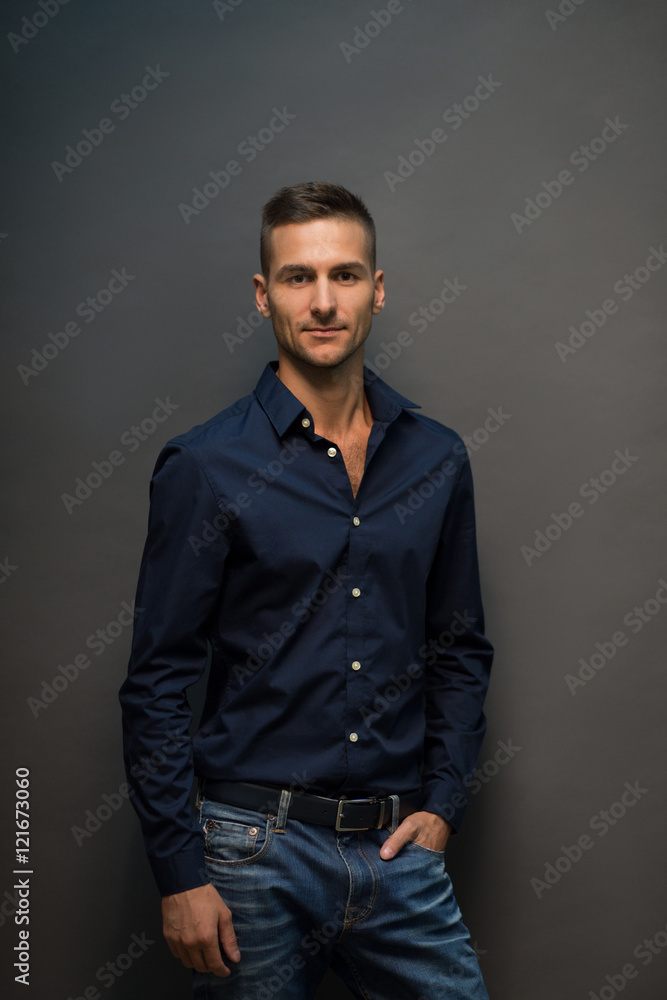 Handsome man in jeans looking at camera and smiling. Fashion or vogue concept. Portrait of model young man in black shirt posing over grey background in studio. Handsome man in jeans looking at camera and smiling. Fashion or vogue concept. Portrait of model young man in black shirt posing over grey background in studio.