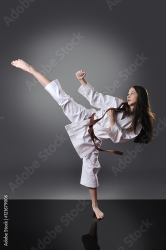 Beautiful young brown belt female karate doing kick on the gray background