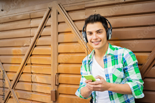 Young millennial guy with headphones and smart phone listening to music