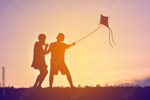 Silhouette children playing kite on sunset