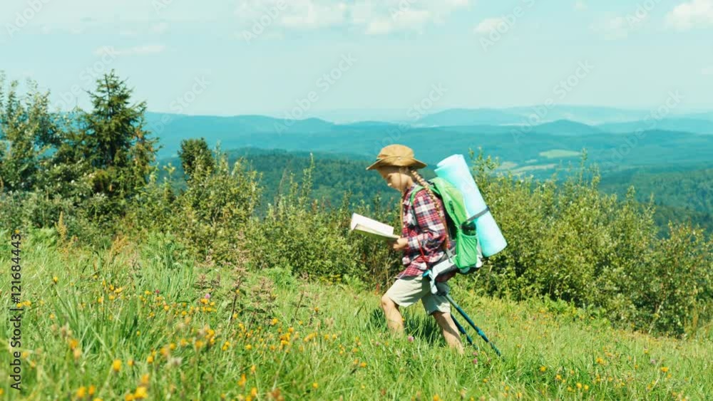 Little hiker girl looking at map and goes up to hill on mountains background and smiling at camera Little hiker girl looking at map and goes up to hill on mountains background and smiling at camera