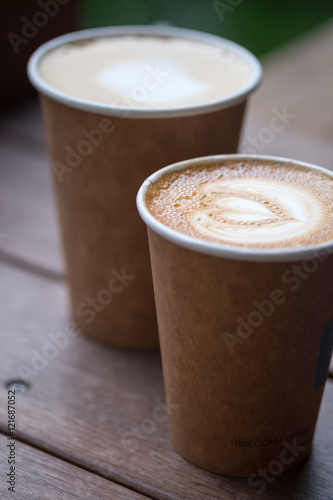 Two cups of latte art with heart shape in brown paper cup. selective focus