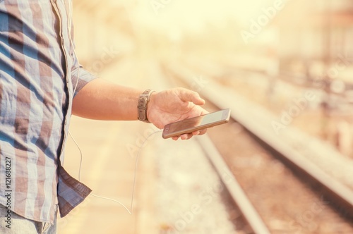 Male tourists are carrying a smartphone headphone jack. Standing near the train tracks, warm tone.