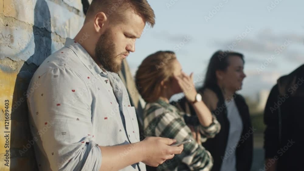 Young Man Using Mobile Phone Outdoors, Group of his Teenager Friends Standing next to Him. Shot on RED Cinema Camera in 4K (UHD). Young Man Using Mobile Phone Outdoors, Group of his Teenager Friends Standing next to Him. Shot on RED Cinema Camera in 4K (UHD).