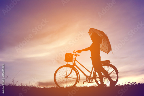 silhouette women with umbrella and bicycle at sunset
