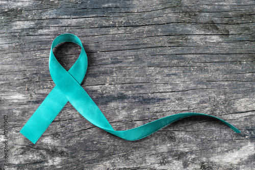 Teal ribbon awareness to support Ovarian Cancer PCOS on human hand with old aged wood background: Satin silk symbolic concept for raising concerns/ help and campaign on people living with illness