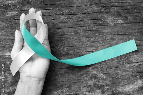 Teal White ribbon awareness support Cervical Cancer on human hand with old aged wood  background: Satin silk ribbon symbolic concept for raising concerns/ help/ campaign on people living with illness photo