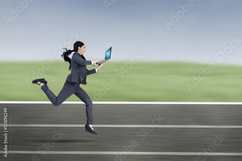 Female entrepreneur with laptop runs on track © Creativa Images