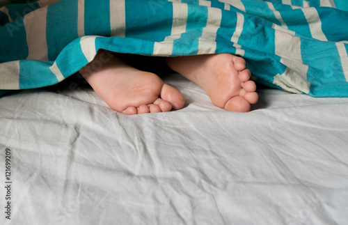 Sleeping feet in bed under blanket.