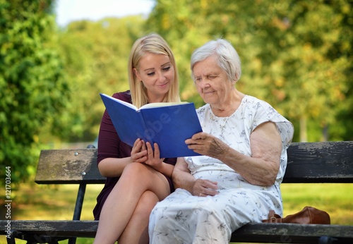 Obraz na płótnie Young woman reading a book elderly woman in the park. w salonie