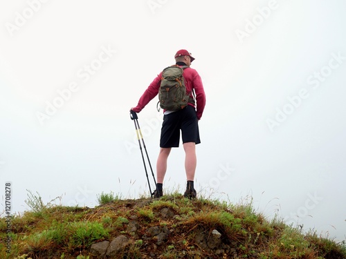 Man in cloud of fog. Hiker in pink black sportswear and poles
