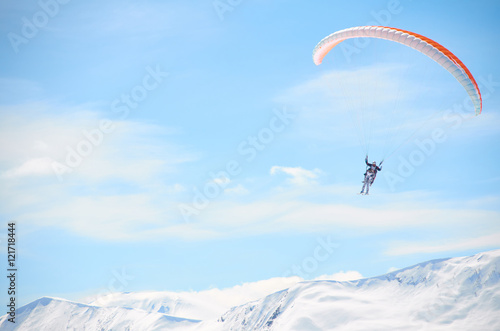 Paragliding high in mountains in blue bright sky. Tandem fly above peaks snowy peaks in sunny day. Extreme sport life. Extreme sport health weekend or holiday outdoor.