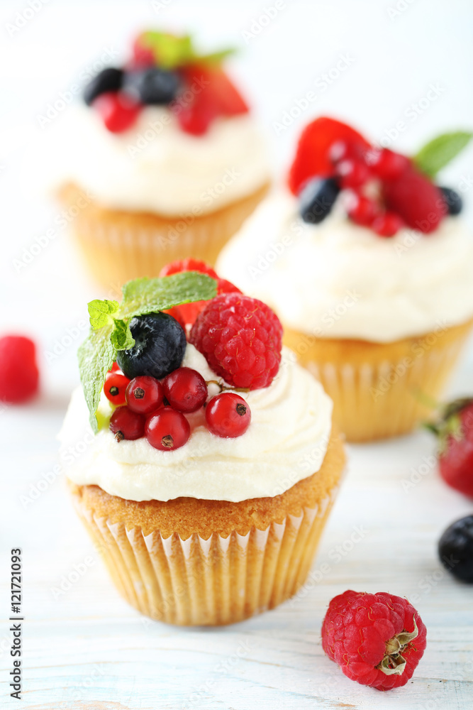 Tasty cupcakes with berries on white wooden table Tasty cupcakes with berries on white wooden table