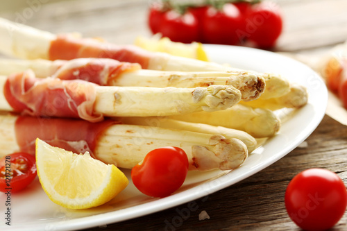 Fresh white asparagus wrapped in jamon on a grey wooden table