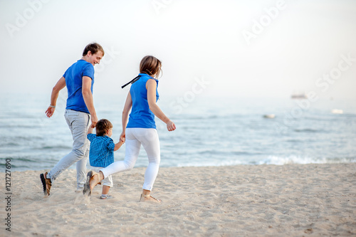 Man woman and child run on the beach near the ocean and feel happy
