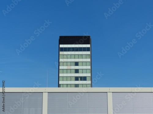 Hochhaus im Stil der Sechziger Jahre und moderne Messehalle vor blauem Himmel im Sonnenschein auf dem Messegelände der Köln Messe im Stadtteil Deutz in Köln am Rhein in Nordrhein-Westfalen photo