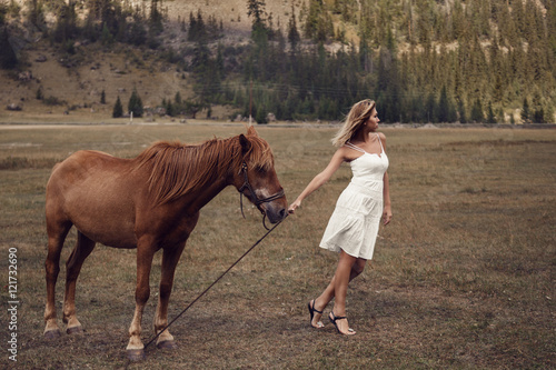 Young beautiful woman in white dress walking with horse