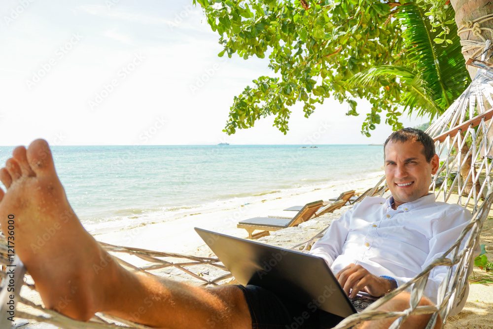 Young man work on laptop relaxing in hammock with seaview