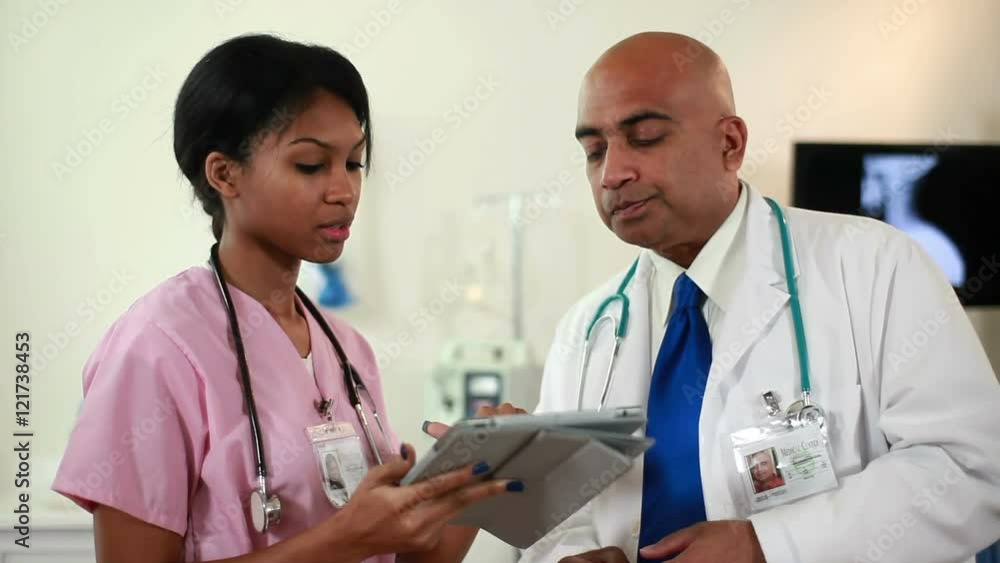 Indian physician and pretty African American nurse review information on electronic tablet. Indian physician and pretty African American nurse review information on electronic tablet.