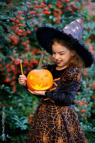 Cute girl of 8-9 years in a suit for Halloween with pumpkin and magic wand into hands.
