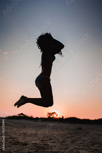 Girl jumping on sand at sunset