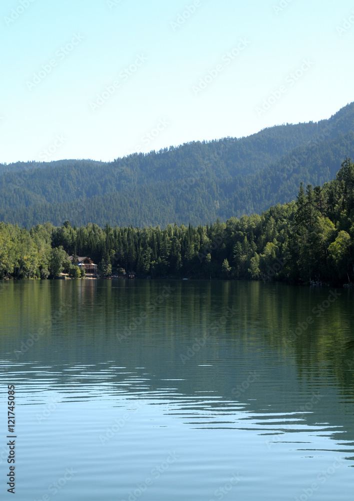 In the clear water of a forest lake reflects the sky, mountain, forest and clouds. Photo partially tinted.