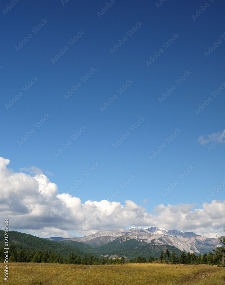 Blue sky and cumulus clouds over the Eastern Sayan Mountains and Mount MunKu-Sardyk. Photo partially tinted.