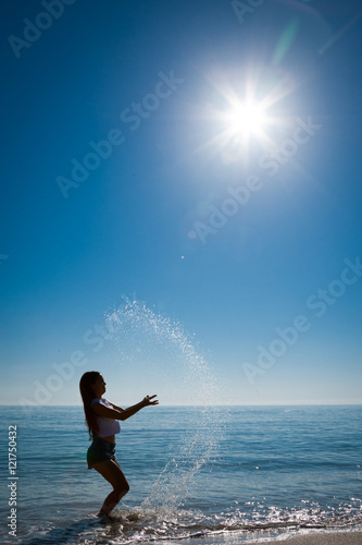 young woman splashes water in air at beach