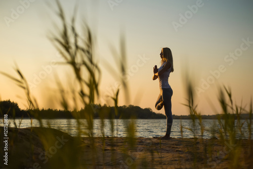 Girl practicing yoga at the water against the sky