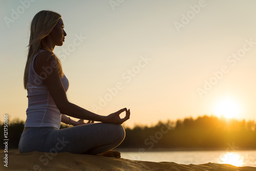 Girl practicing yoga at the water against the sky