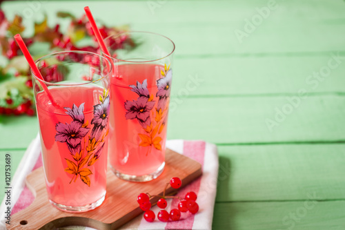 Fresh viburnum drink in glass on green wooden background with leaves and berries. Selective focus.