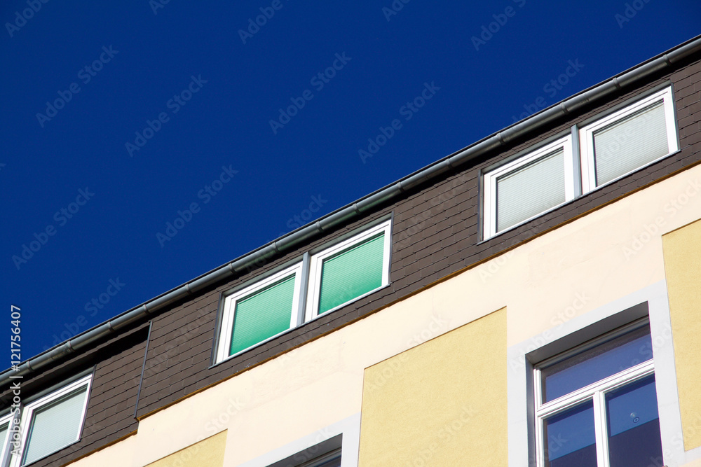 Facade of a yellow house with windows with closed shutters in different colors. Against a blue sky with copyspace. Aachen, Germany