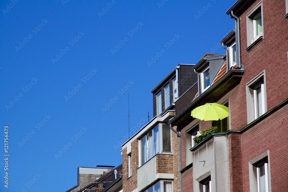 Row of houses, one with a sunshade on balcony for a relaxed evening, against a blue sky in Aachen, Germany
