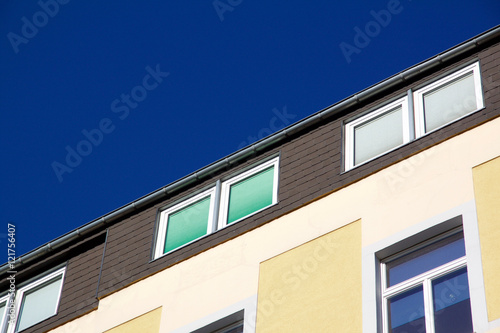 Facade of a yellow house with windows with closed shutters in different colors. Against a blue sky with copyspace. Aachen, Germany