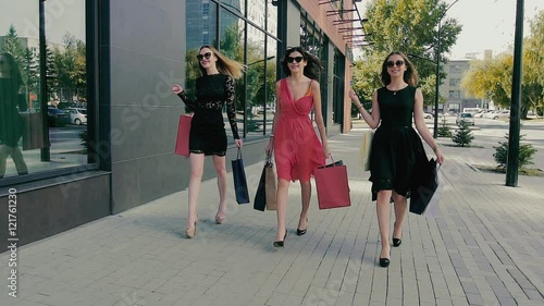 Group of attractive young women walking along shop windows. Slow motion
