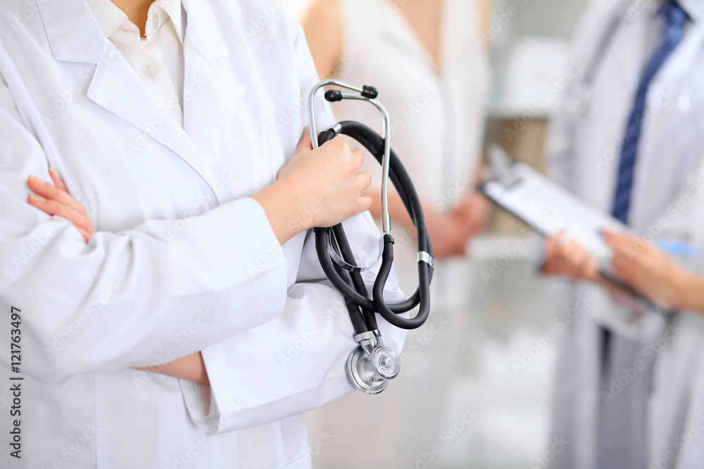 Female doctor holding a stethoscope in his hand, two doctors and patient are on the background Female doctor holding a stethoscope in his hand, two doctors and patient are on the background