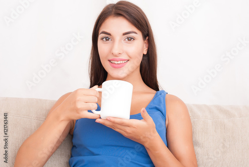 young brunette woman sitting on couch and drinking coffee