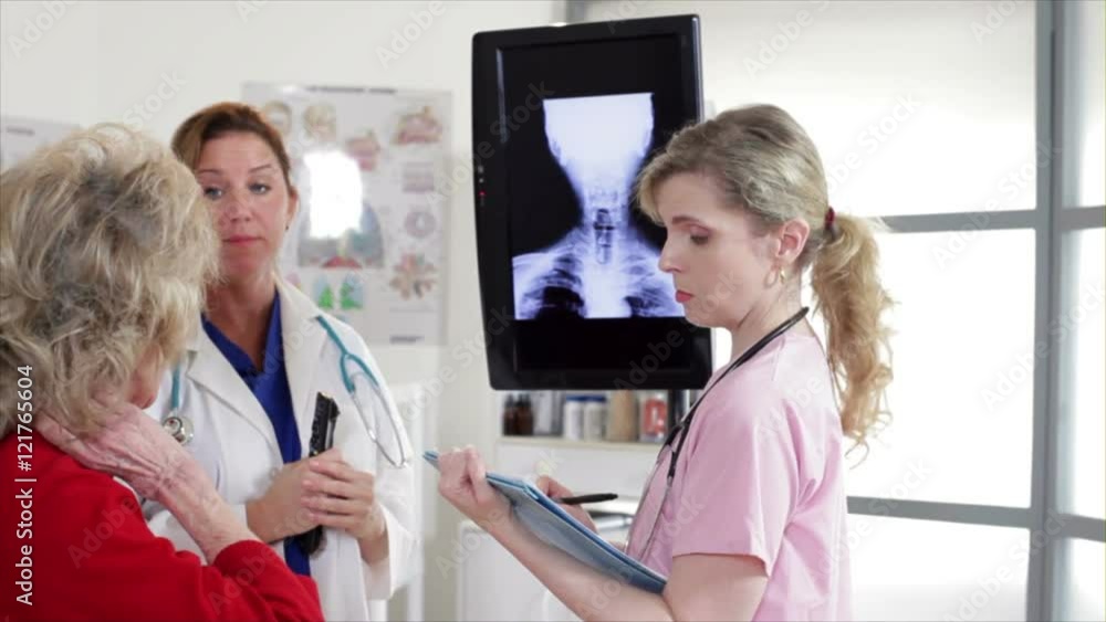 A doctor and her nurse discuss with an elderly patient the x-rays displayed on a monitor. A doctor and her nurse discuss with an elderly patient the x-rays displayed on a monitor.
