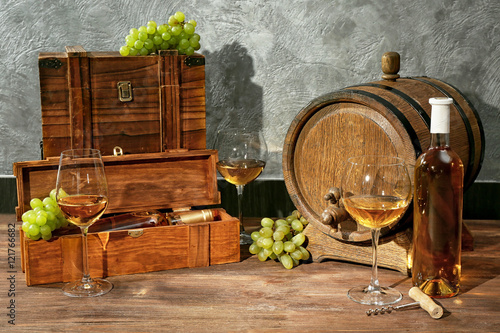 Glasses of white wine, grapes, box and barrel on a wooden table