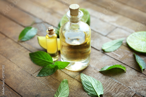 Bottles with mint oil, lime and fresh leaves on wooden background