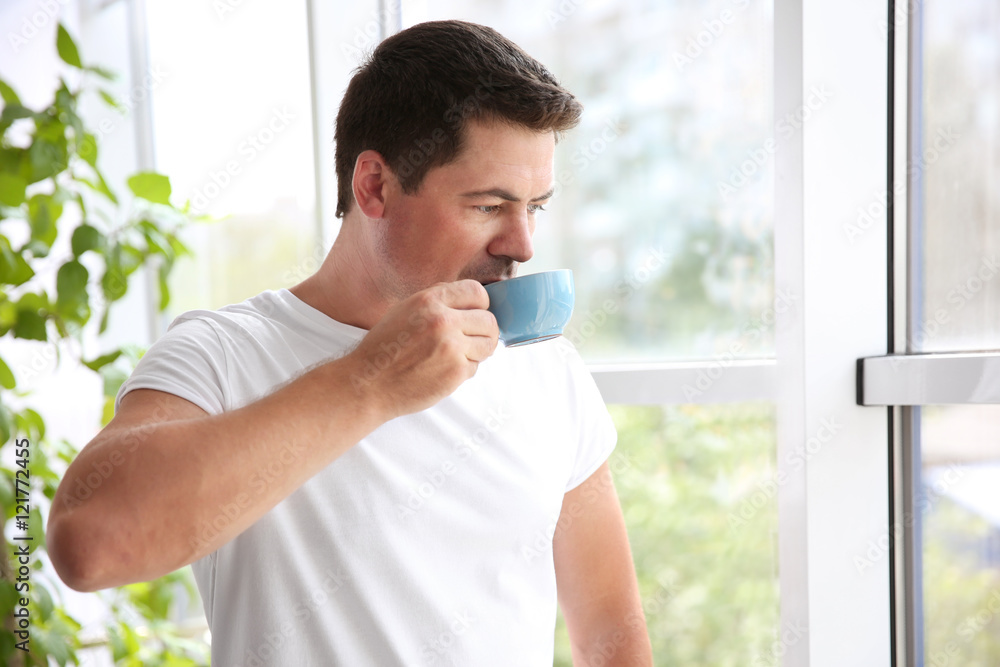 Handsome man standing near window with cup of morning coffee