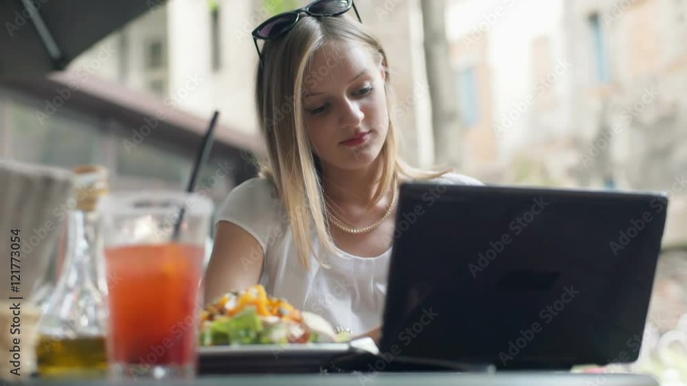 Businesswoman working on laptop and smiling to the camera in the outdoor cafe
Businesswoman working on laptop and smiling to the camera in the outdoor cafe