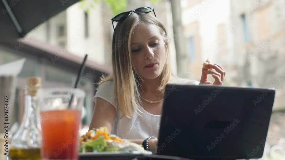 Businesswoman eating her lunch and working on laptop in the outdoor cafe
Businesswoman eating her lunch and working on laptop in the outdoor cafe