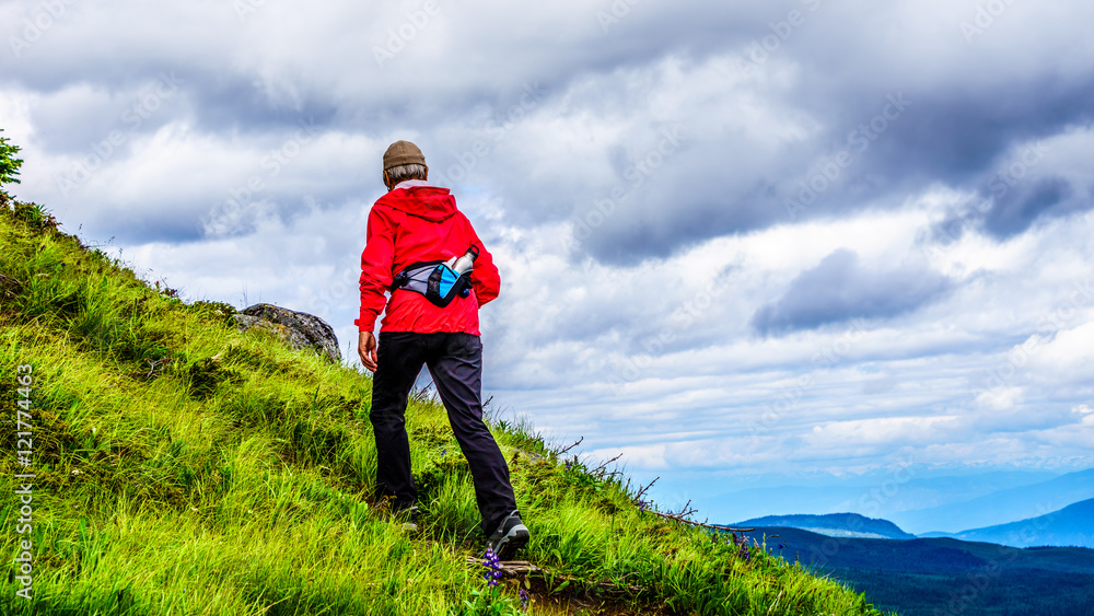 Senior Woman in a red jacket hiking up a steep slope on a hike to Tod Mountain in the Shuswap Highlands of British Columbia, Canada