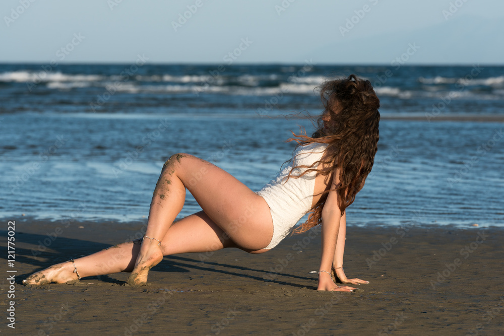 Woman with long curly hair and excellent body wear white monokini, make a dance moves at the beach. Sea and sky as background Woman with long curly hair and excellent body wear white monokini, make a dance moves at the beach. Sea and sky as background