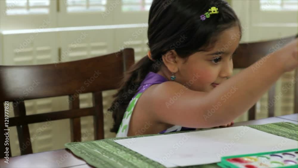 A cute little Indian child sitting contentedly by a large shuttered window starts to paint with her watercolors. Camera pans down. A cute little Indian child sitting contentedly by a large shuttered window starts to paint with her watercolors. Camera pans down.