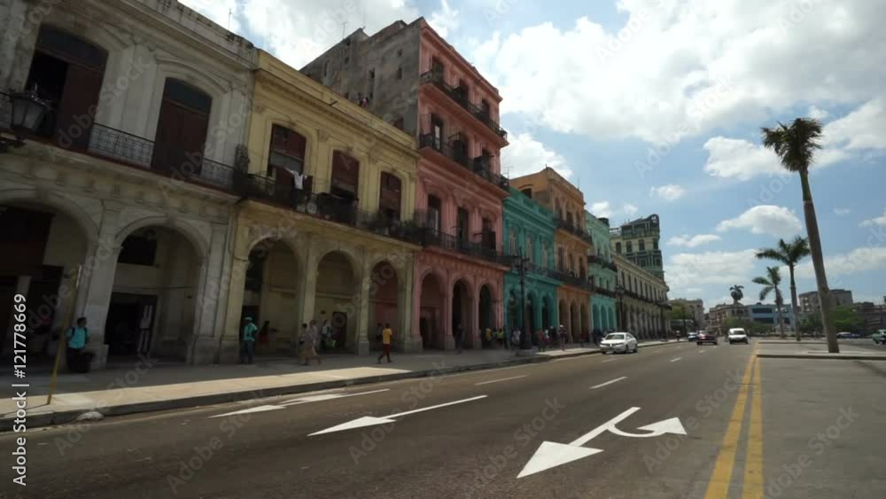 Famous street in Havana of multi-colored houses with big arches. Bright colorful retro cars are passing by at summer cloudy day. Famous street in Havana of multi-colored houses with big arches. Bright colorful retro cars are passing by at summer cloudy day.